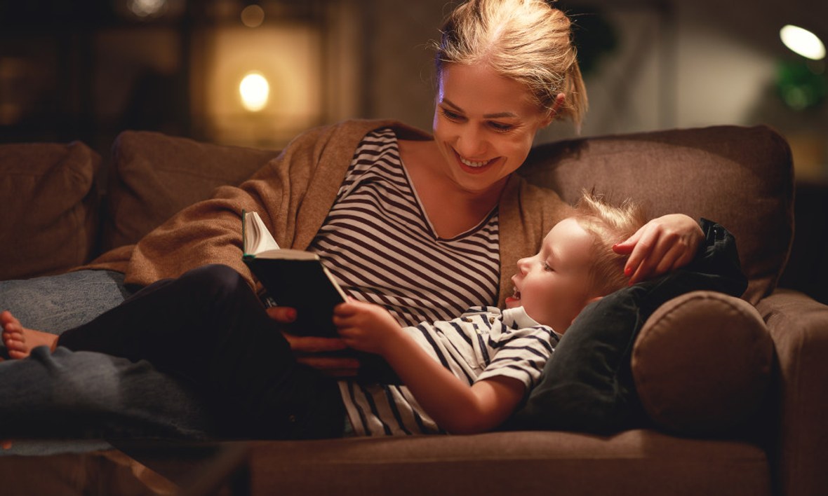 Mutter und Kind liegen auf dem Sofa und lesen ein Buch