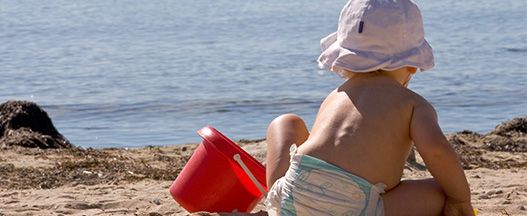 Baby am Starnd mit rotem Eimer und Schaufel