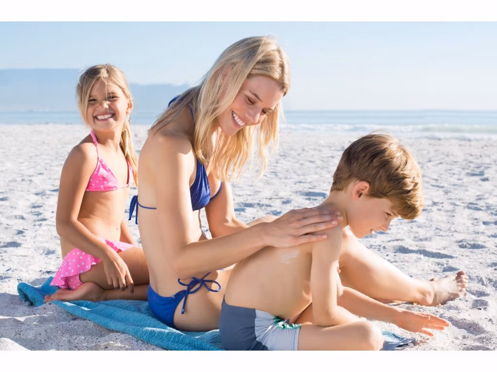 Mutter cremt Kinder am Strand mit Sonnencreme ein