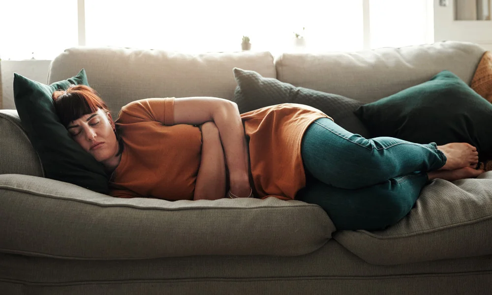 Frau liegt mit Bauchschmerzen auf dem Sofa