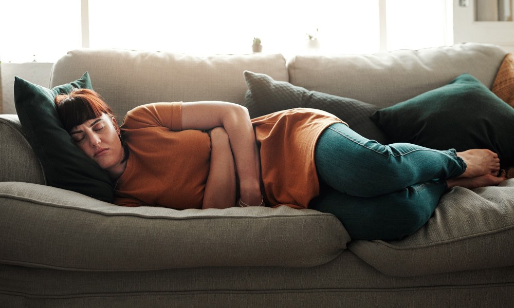 Frau liegt mit Bauchschmerzen auf dem Sofa