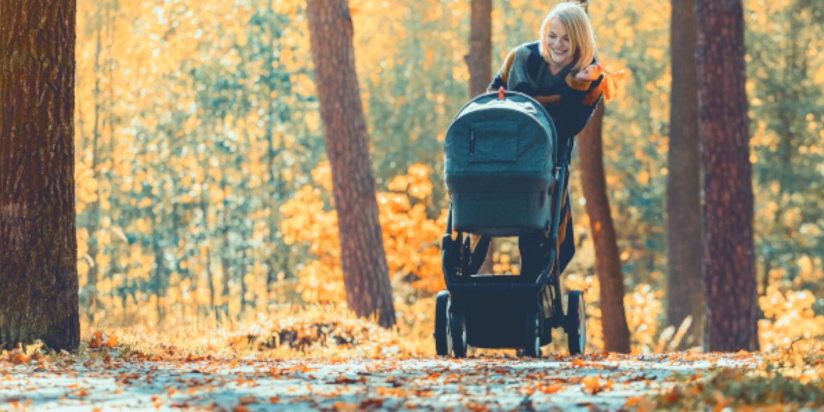 Junge Frau geht im Herbst mit Baby und Kinderwagen spazieren.
