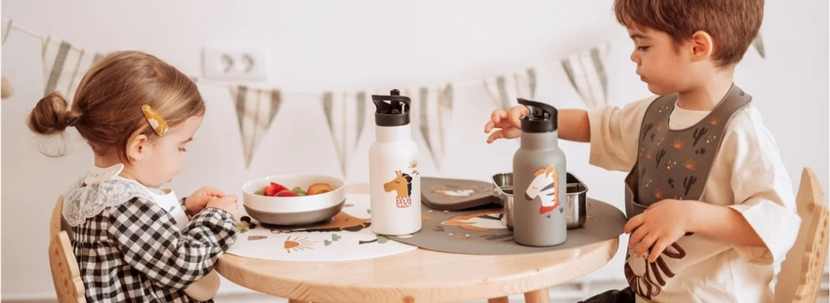 Kinder sitzen am Tisch und haben edle Edelstahl Trinkflaschen aus denen sie trinken können.