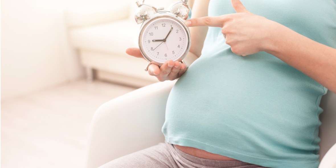 Hochschwangere Frau tippt auf Uhr und drängelt