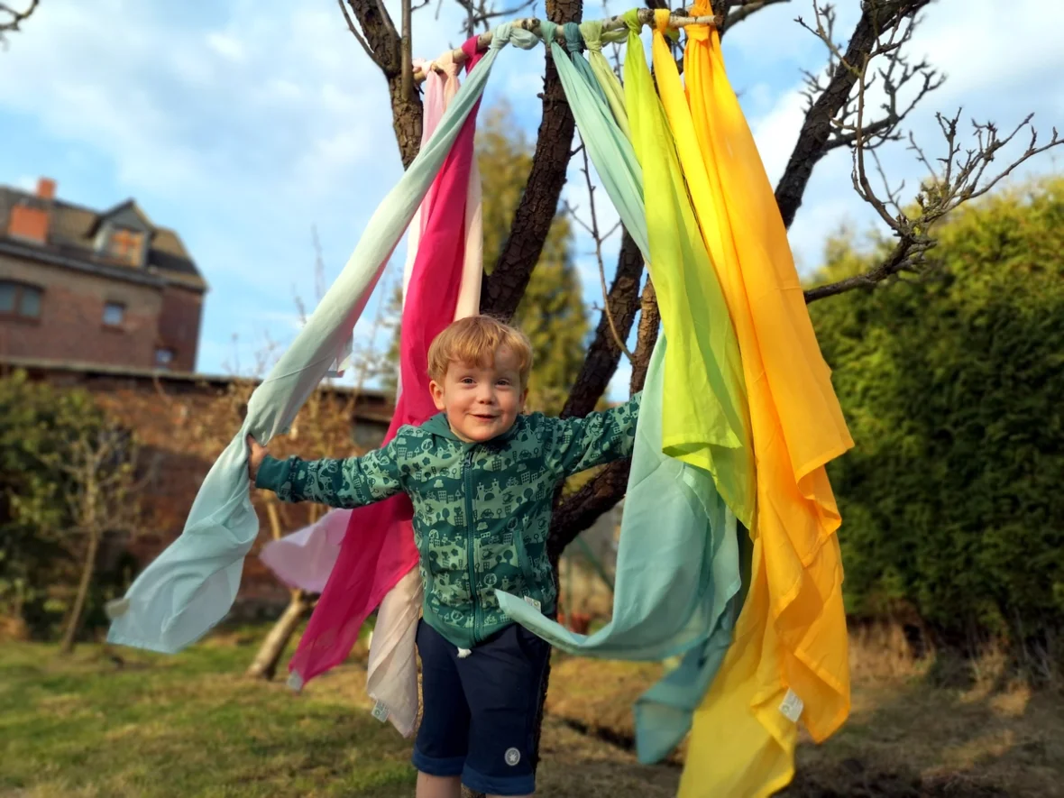 Kleines Kind versteck sich hinter Spieltüchern, die den Eingang für die Höhle darstellen.