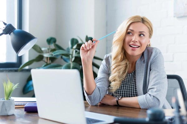 Lächelnde Geschäftsfrau hält Bleistift in der Hand und schaut bei der Arbeit weg