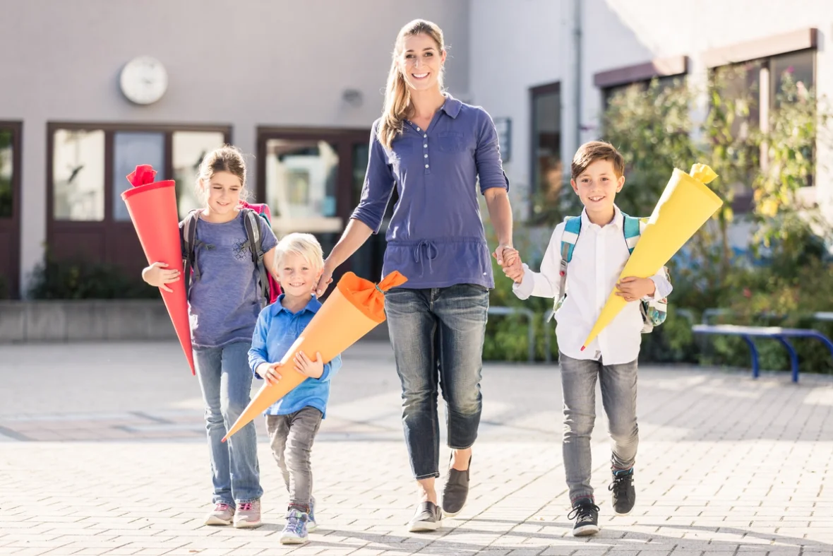 Mutter mit 3 Kindern. Alle haben eine Schultüte in der Hand und freuen sich auf dem Weg zur Schule.