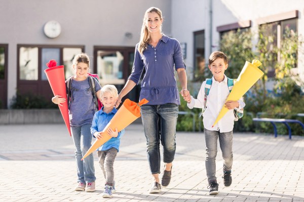 Mutter mit 3 Kindern. Alle haben eine Schultüte in der Hand und freuen sich auf dem Weg zur Schule.