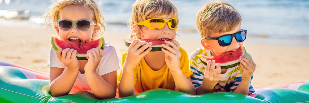 Children eat watermelon on the beach in sunglasses