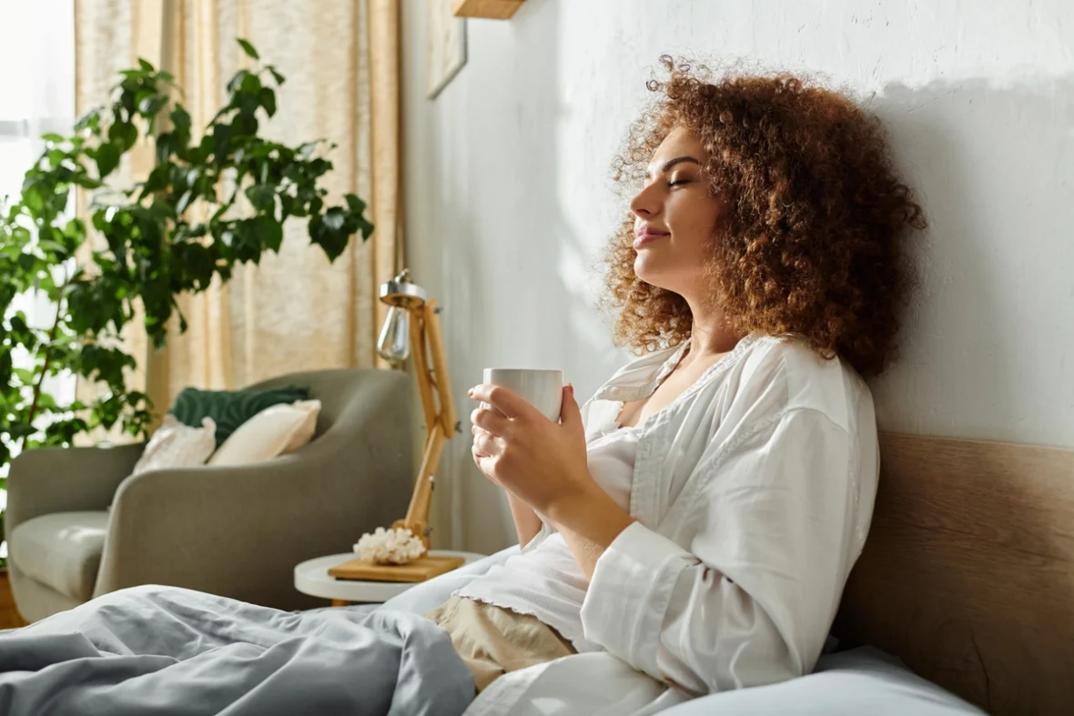 Eine Frau wirkt sehr entspannt mit einer Tasse Tee in der Hand zugedeckt auf dem Sofa