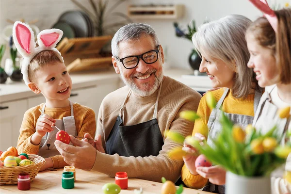 Familie sitzt zusammen am Tisch und hat Spaß beim Ostereier bemalen