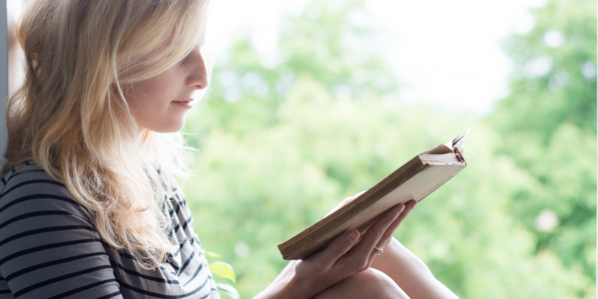 Frau sitzt auf Fensterbank und liest ein Buch.