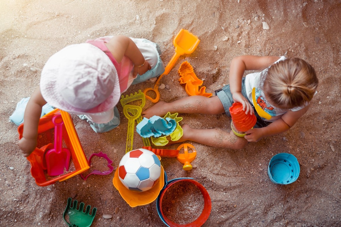 Kinder sitzen im Sand und spielen mit Sandspielzeug