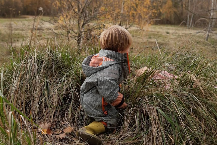 Ein Junge sitzt draußen in der Natur mit Gummistiefel und Regenjacke bei trübem Wetter.