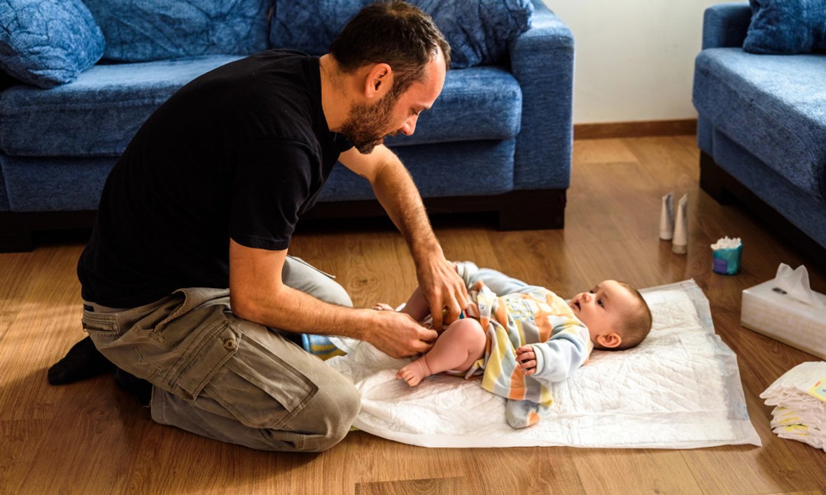 Vater wickelt Baby auf dem Fußboden im Wohnzimmer