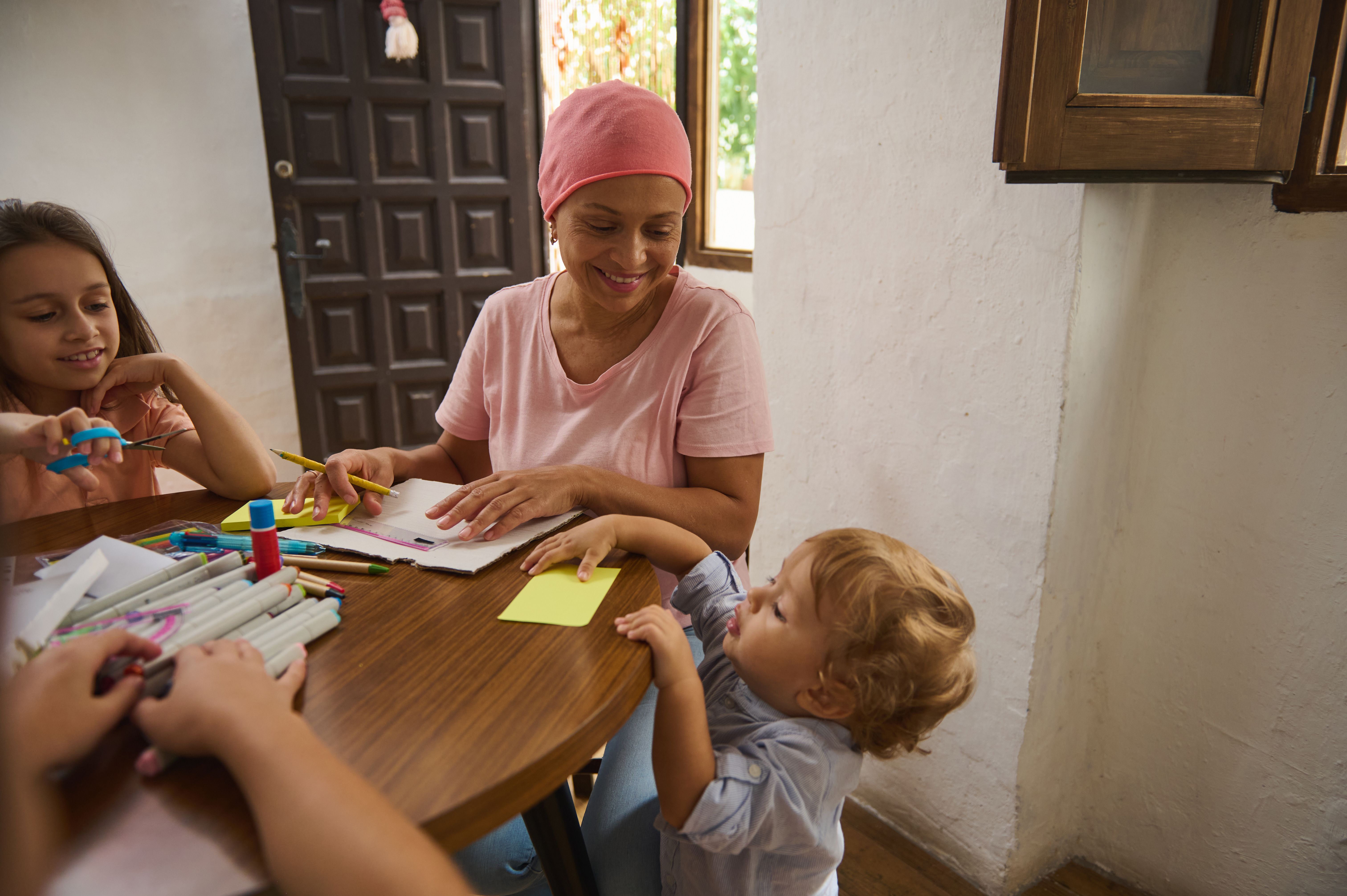 Mutter sitzt mit ihrer Familie am Tisch und sie arbeiten fröhlich mit Stift und Zetteln.