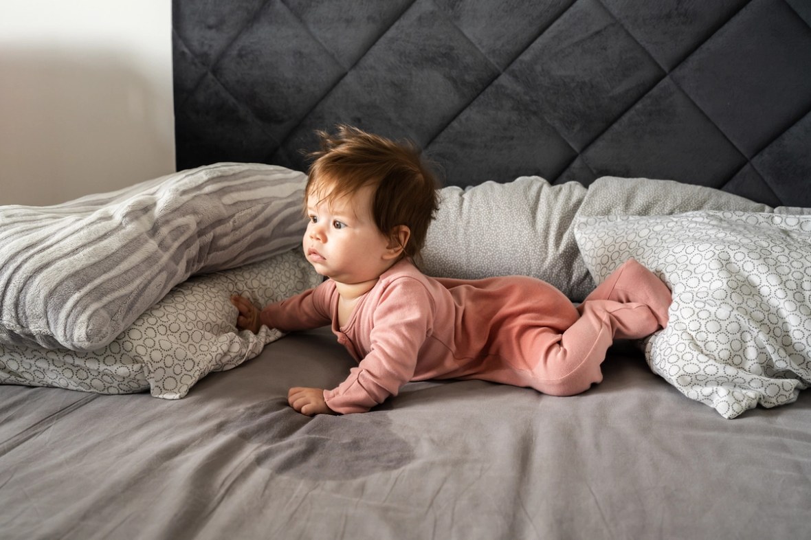 Baby auf dem Bett. Urinfleck auf dem Laken.