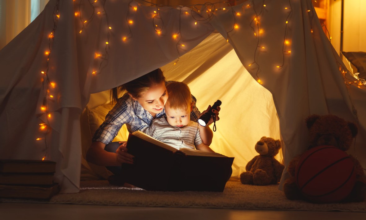 Mutter und Kind lesen in einer Höhle mit Lichterketten ein Buch