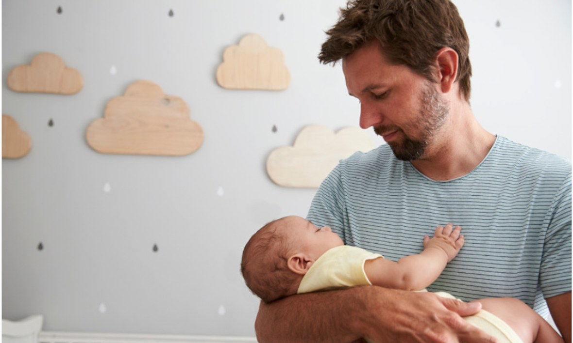 Vater hält schlafendes Baby im Arm.