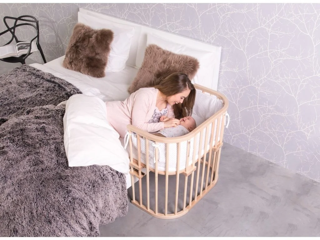 Mutter liegt im Bett und das Baby daneben im Babybay Beistellbett