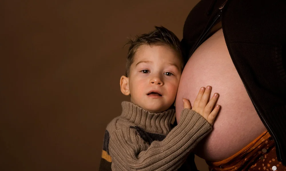 Junge horcht am Babybauch seiner Mutter