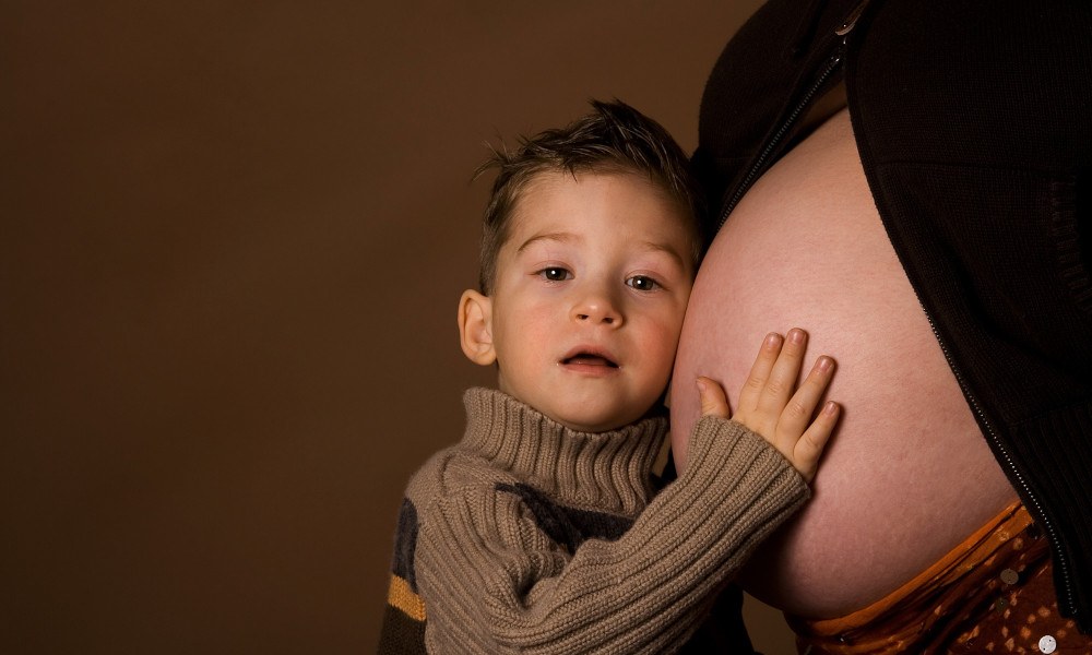 Junge horcht am Babybauch seiner Mutter